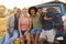 Portrait Of Friends Sitting On Tailgate Of Pick Up Truck On Road Trip To Cabin In Countryside