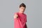 Portrait of frowning teenager boy and pointing finger to the camera and to you, wearing casual pink t shirt, standing over gray