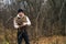 Portrait of frozen tourist male wearing warm clothes collecting dry deadwood for fire in forest on overcast cold day.