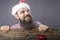 Portrait of a funny bearded man with santa cap holding a red round decoration ball