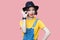 Portrait of funny beautiful young woman in yellow t-shirt and blue denim overalls with makeup and black hat standing with ok sign