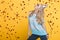 Portrait of funny blond woman in birthday hat and red confetti on yellow background. Celebration and party.