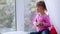 Portrait of funny cute little girl sitting on window sill and eating apple.