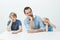 Portrait of funny family of father and sons sitting at table, leaning head on hand and making faces at camera, being