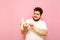 Portrait of a funny fat man in a white T-shirt on a pink background, reveals a banana and looks hungry for fruit. Cheerful young