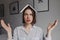 Portrait of funny girl who crosses her eyes and poses with book on her head against background of white room with