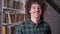 Portrait of funny handsome man standing in library and smiling at camera, bookshelves with books in background