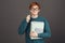 Portrait of funny handsome redhead teen in green fashionable sweater holding notebooks in hand, looking with popped up