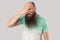 Portrait of funny middle aged bald man with long beard in light green t-shirt standing and looking through his fingers, cunning,