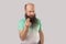 Portrait of funny middle aged bald man with long beard in light green t-shirt standing with money or italian gesture and looking