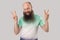 Portrait of funny middle aged bald man with long beard in light green t-shirt standing with victory or peace gesture and looking