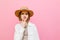 Portrait of a funny pensive girl in a hat, looking at the camera and thinking on a pink background. Attractive lady in pensive