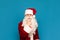 Portrait of a funny pensive teenager in Santa Claus costume, looking intently into the camera, isolated on blue background. Young