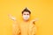 Portrait of a funny puzzled student in a medical mask and a book on his head, posing at the Khmer on a yellow background. Home