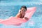 Portrait of funny satisfied female swimming in swimming pool with help of pink water mattress, relaxing with closed eyes and