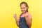 Portrait of funny smiling little girl with braid in denim overalls gesturing i need cash, child demanding pocket money