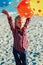 Portrait of funny white Caucasian child kid boy with colorful bunch of balloons, playing running on beach on sunset