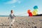 Portrait of funny white Caucasian child kid with colorful bunch of balloons, playing smiling on beach on sunset