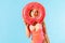 Portrait of funny woman in swimsuit looking through big donut rubber ring, sending air kiss with pout lips