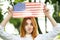 Portrait of funny young red haired woman holding USA national flag in her hands standing outdoors in summer park. Positive girl