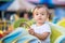 Portrait of future racing champion: toddler child sitting on little bright car on merry-go-round in theme park with proud face