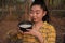 Portrait gardener young asea woman look at a full cup of raw para rubber milk of tree in plantation rubber tapping form Thailand,