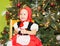 Portrait of girl child in suit a red hat for Christmas around a fir-tree decorated. Kid on holiday new year