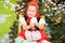Portrait of girl child in suit a red hat for Christmas around a fir-tree decorated. Kid on holiday new year