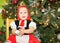 Portrait of girl child in suit a red hat for Christmas around a fir-tree decorated. Kid on holiday new year