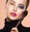 Portrait of a girl with cosmetic brush near face. Woman making makeup on the face using makeup brush. One half face of a beautiful