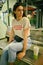 Portrait of girl with dark sunglasses on her head posing sitting on bench in shopping mall. Dressed in white t-shirt