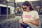 Portrait of a girl in dark sunglasses posing near a city mall. Dressed in white t-shirt, blue trousers, black waist bag