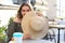 Portrait of a girl hiding her face behind a straw hat while sitting in summer street cafe