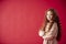 Portrait Of Girl With Long Red Hair Against Red Studio Background Smiling At Camera And Folding Arms