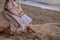 Portrait of a girl near the sea sitting on the rocks with a toy ship in hands.