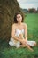 Portrait of a girl with short black hair in a bright white dress amongst haystacks in a green field.