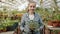 Portrait of girl standing inside greenhouse holding pot plant smiling and looking at camera