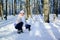 Portrait of a girl in white hat and scarf outside sitting near funny snowman. Blue sky and frosty trees on background.