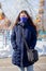 Portrait of a girl in a winter jacket with a hood and in a blue protective mask on her face strolling through a deserted amusement