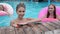 Portrait girls swimming with pink inflatable rings in poolside, friends swim into swimming-pool with blue water