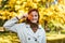 Portrait of glad caucasian millennial red haired female in raincoat puts yellow leaf to her eye