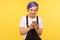 Portrait of glad hipster girl using cell phone, texting or reading message with good news. yellow background, indoor studio shot