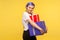Portrait of glad positive hipster girl carrying gift boxes and smiling at camera. yellow background, indoor studio shot