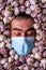 Portrait of a gloomy man in a blue medical mask and closed eyes among garlic bulbs