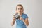 Portrait of good-looking blond girl in blue t-shirt holding camera in hands with concentrated expression, going to take