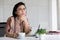 Portrait of good looking and kindly warm feeling Asian senior woman wearing eyeglasses sitting and drinking coffee at working desk