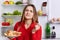 Portrait of good looking young female frowns face as smells tasty sandwhiches, stands in kitchen with food near opened fridge full