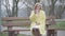 Portrait of gorgeous lonely blond woman sitting on bench and drinking coffee. Young Caucasian lady in yellow coat