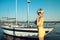 Portrait of gorgeous middle-aged blond woman wearing yellow tight-fitted lace mini dress and sunglasses standing on the yacht pier