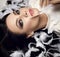 Portrait of graceful brunette woman vamp with perfect evening makeup lying on floor surrounded with white feather